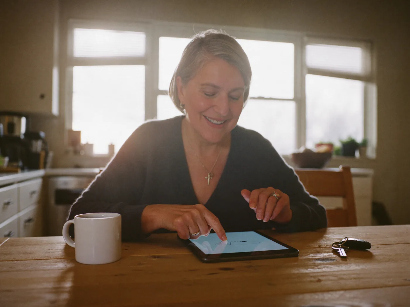 A homeowner at a sunlit kitchen table tapping a tablet to sign her window agreement